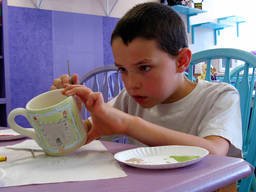 A young boy shows full attention as he paints his ceramic mug.