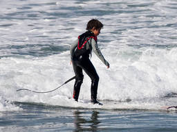 A young boy in full gear surfs near the shore.