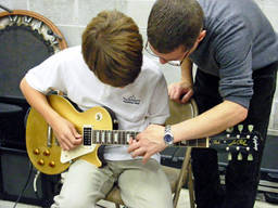 A kid being taught by his teacher to play guitar