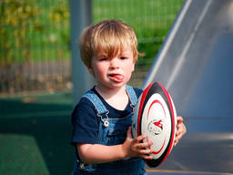 A toddler holds onto a football after playing pass with his friends