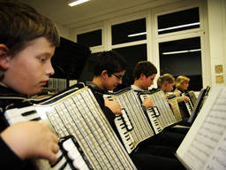 Kids playing accordion, with the teacher at the far side