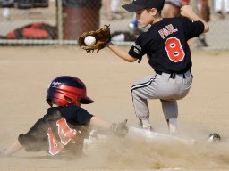 A young boy hits the base safely just as the ball is caught by the opposing player.